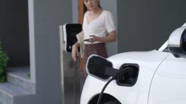 Evinde şarj edilen elektrikli bir araçla işten yeni dönen modern bir kadının ilerici yaşam tarzı. Elektrikli araç, sürdürülebilir temiz enerjiyle çalışıyor..