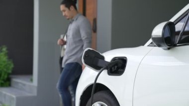 Adamın biri evinde elektrikli araç şarj aletinin fişini çekiyor. İlerici bir yaşam tarzında elektrikli araçların kullanımı, temiz ve sağlıklı bir çevreye katkıda bulunur..