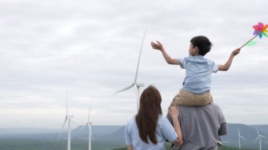 İlerici mutlu aile kavramı rüzgâr türbini çiftliğinde eğleniyor. Rüzgar türbini jeneratörüyle gelen elektrik jeneratörü kırsal bölgede tepe ve ufukta dağ var..