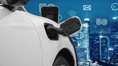 5G Network dijital hologramı ve internet tabelaları gece şehrinin arka planında beliriyor. Çevre koruma kavramı için kablo prizi olan şarj istasyonuna bağlı ilerici elektrikli araç.