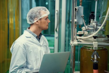 CBD yağ çıkarıcısının yanında dizüstü bilgisayarla çalışan eczacı bilim adamı ve tıbbi esrar ürünleri üretmek için kullanılan bilimsel bir makine.