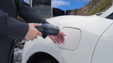 İş dünyasındaki ilerici adam elektrik yükleme istasyonundan doğal şelale ve akış geçmişi olan elektrikli araba giyer. Enerji sürdürülebilirliği kavramı.