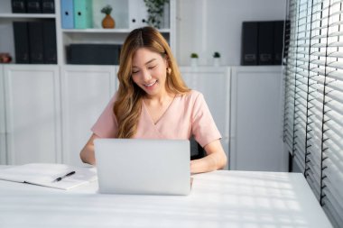 A young Asian female employee sitting at her desk in her office, sitting at desktop in workstation.