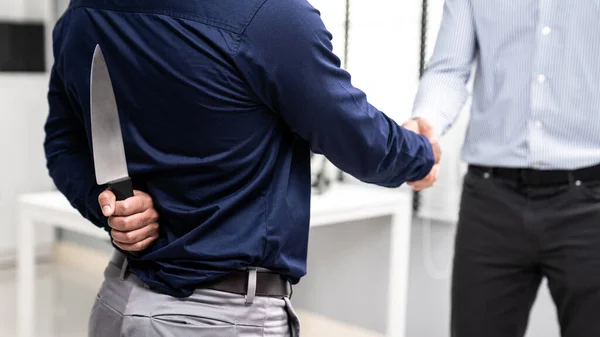 Back view of businessman shaking hands with another businessman while holding a knife behind his back. Concept of back backstabbing in business, backstabbing between colleagues.