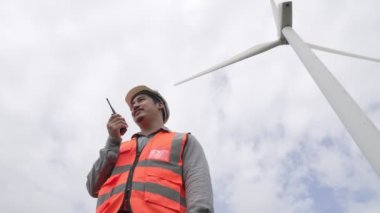 Gökyüzü arka planına sahip bir rüzgar türbini üzerinde çalışan mühendis. Yenilenebilir ve sürdürülebilir enerjinin gelecekteki üretimi için yenilikçi bir ideal. Rüzgar türbininden enerji üretimi.