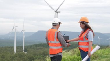 Erkek ve kadın mühendisler kırsal kesimdeki bir tepenin tepesinde ya da dağda rüzgar çiftliğinde çalışıyorlar. Yenilenebilir ve sürdürülebilir enerjinin gelecekteki üretimi için yenilikçi idealler.