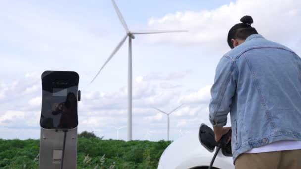 电动汽车是一个进步的人 他的电动汽车 电动汽车用风力涡轮机作为未来可持续能源的概念 从绿地的充电站向能源充电 配备发电机的电动车 — 图库视频影像